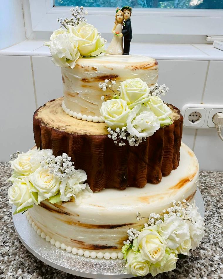 Kétemeletes esküvői torta fatörzs-mintás középső emelettel és fehér rózsákkal