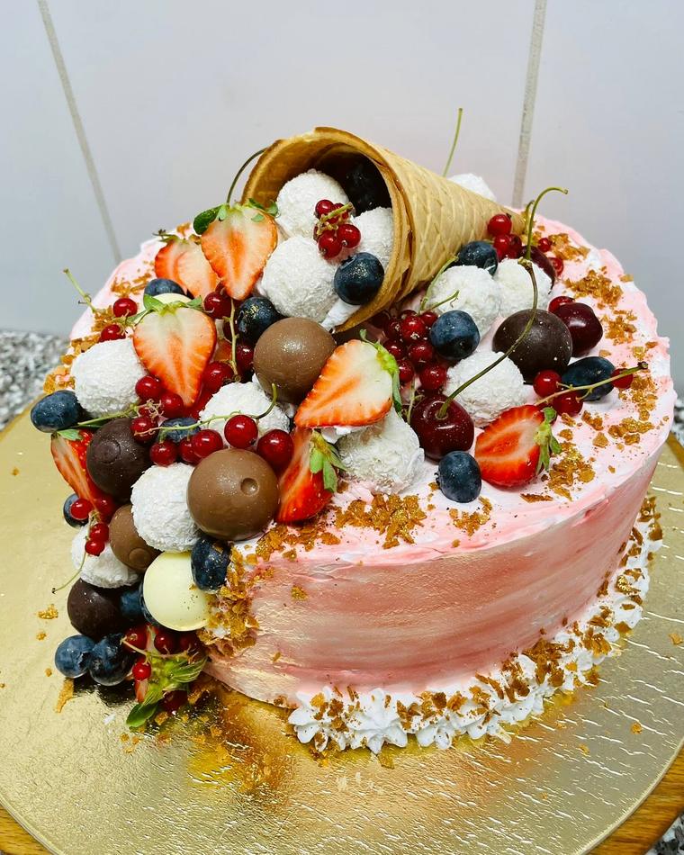 Rózsaszín torta bogyós gyümölcsökkel, csokoládégolyókkal és ostyatölcsérrel